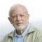 Пожилой мужчина с белой бородой улыбается на светлом фоне.